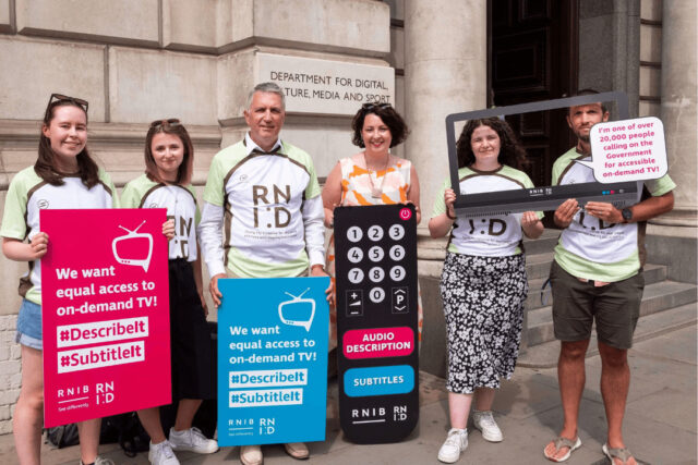 A group of six campaigners standing in front of a building, holding placards