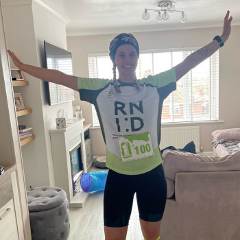 Woman wearing cycling gear and an RNID running tshirt, holding out her arms and smiling.