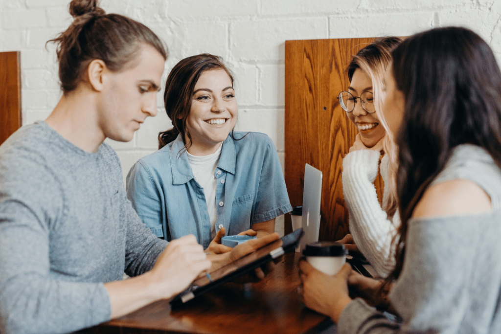 Four people around a table with laptops, pens and coffee cups, smiling