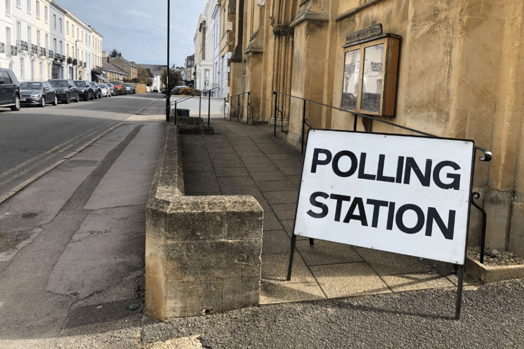 A photograph of a street in the UK with a road sign saying: "POLLING STATION" outside of an old building.