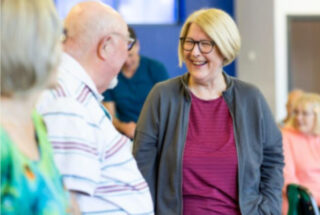 A man and a woman talking to each other and laughing, in a community hall.