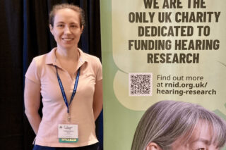 Dr Magdalena Zak stands beside an RNID banner.