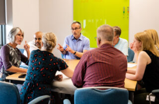 A group of work colleagues seated around a meeting room table, in discussion.