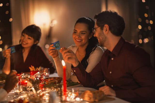 A group of people around a Christmas dinner table, looking at RNID Christmas Dinner Game cards and smiling.