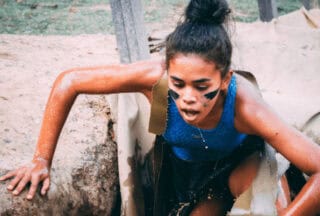 A woman with warpaint climbing out of a muddy hole on an obstacle course