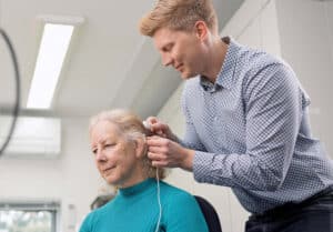 A healthcare professional fitting a woman with a cochlear implant.