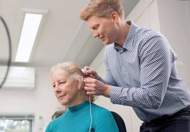 A healthcare professional fitting a woman with a hearing aid