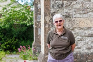 An RNID volunteer stands outside in a garden and smiles at the camera