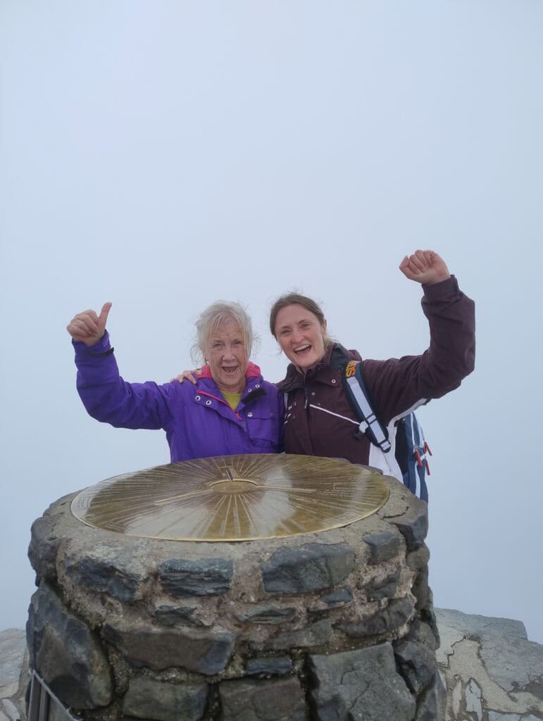 Two women stand at the top of Snowdon celebrating.