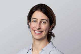 A woman in a grey shirt smiling at the camera.
