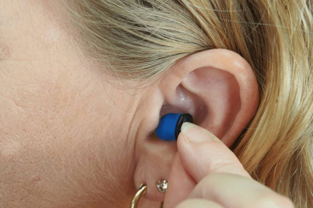 A close up of a woman's ear. She's putting an earplug in.