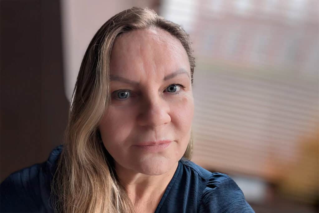 A woman with long blonde hair wearing a blue blouse.
