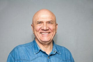 A bald man in a blue t-shirt smiles at the camera.