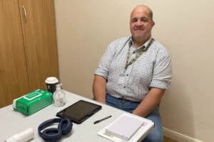 RNID volunteer, Barry, sits behind a desk. He is smiling.