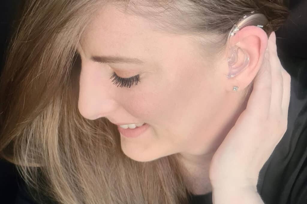 Rachel, in side profile, looks down to the floor. She moves her hair to one side so her cochlear implant is visible.