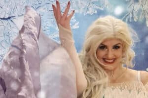 A woman dressed as a fairy tale princess with long blonde hair smiles.