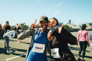 Two women taking part in a running challenge have their arms around each other and are smiling.