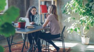 Two women seated at a table in an office, one has a laptop