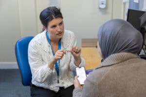 An audiologist sits with a patient and helps them with a hearing aids app.