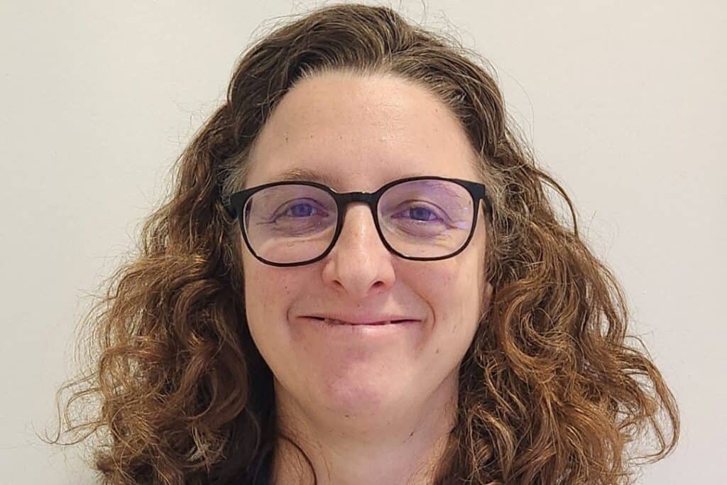 A headshot of RNID-funded researcher, Marcela. She has curly brown hair and wears glasses.