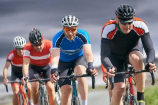 A group of people cycling together. They wear Lycra and cycling hats.