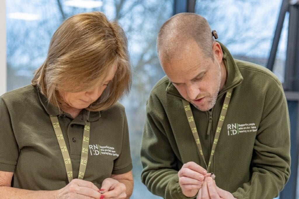 Two RNID Near You volunteers examine a faulty hearing aid.